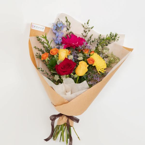 Mixed bouquet of roses, gerbera daisies, and other blooms wrapped in paper