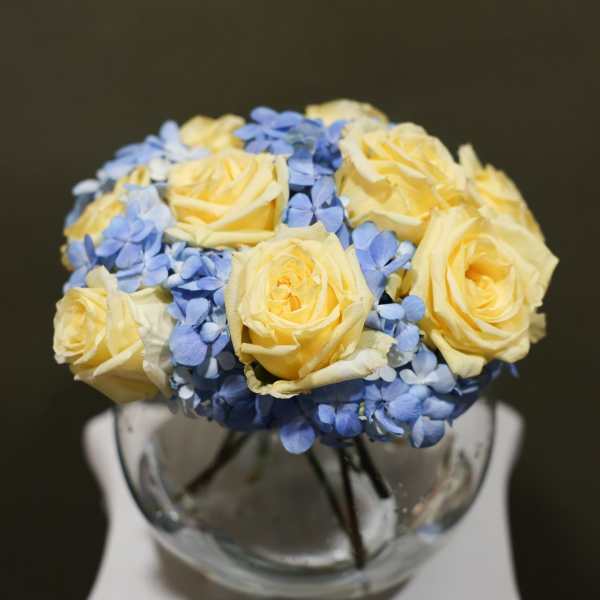 Yellow roses and blue hydrangeas arranged in a glass vase