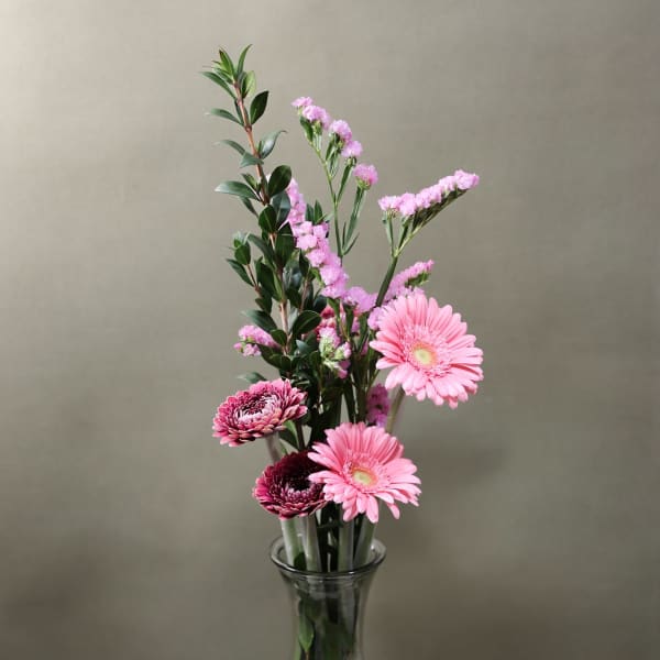 Pink gerbera daisies and small pink filler flowers in a clear glass vase