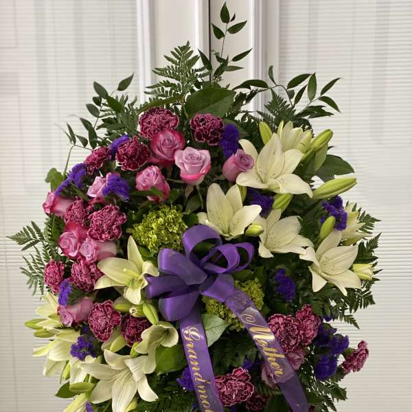 Standing floral wreath with white lilies, pink roses, and purple ribbon