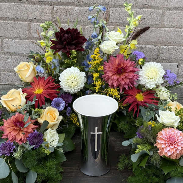 Colorful floral arrangement around a black urn with a cross