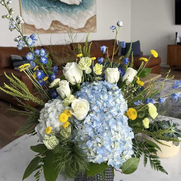 Blue and white floral arrangement with roses, hydrangeas, and yellow accents in a vase