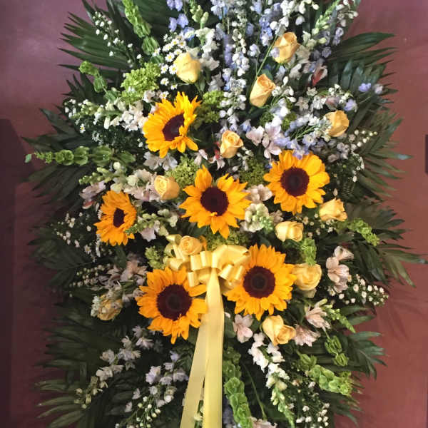 Standing floral spray with sunflowers, yellow roses, and a yellow ribbon