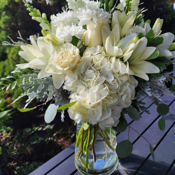 White floral bouquet in a clear glass vase with tall blooms and round greenery