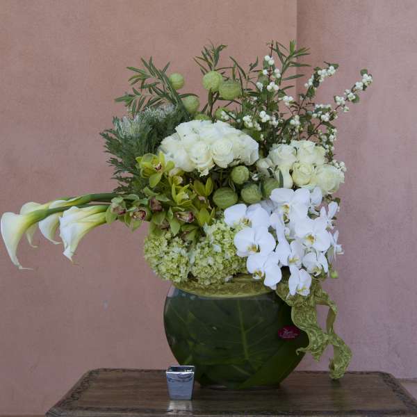 White floral arrangement in a green glass vase with calla lilies and orchids