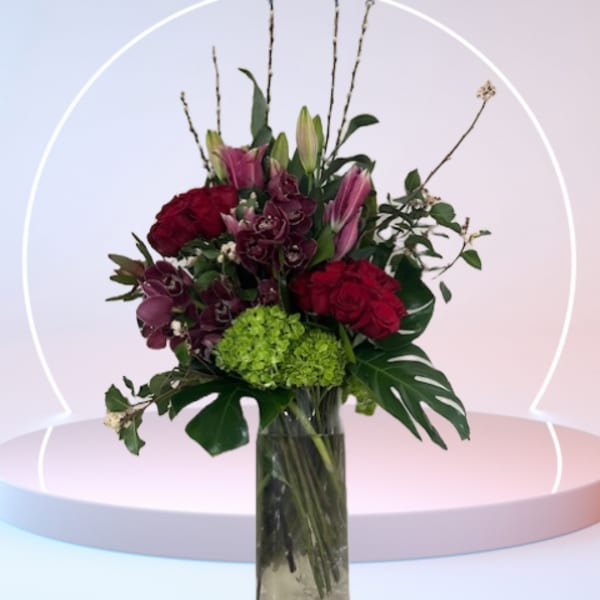 Bouquet of red roses, pink lilies, and green hydrangea in a tall glass vase