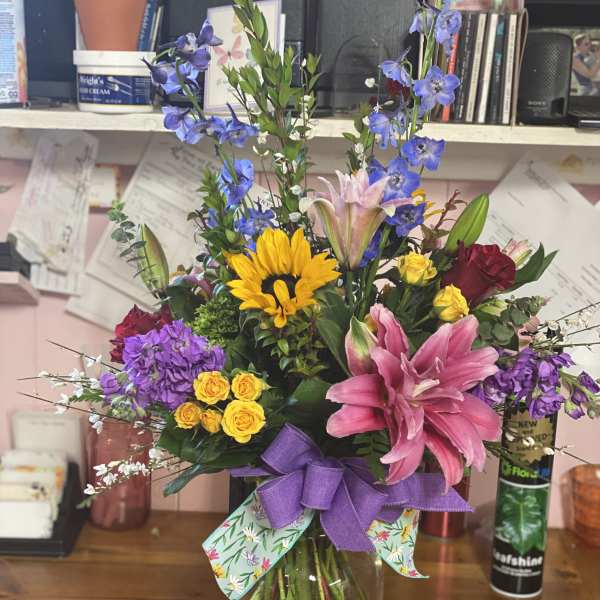 Colorful mixed bouquet in a glass vase with a purple ribbon