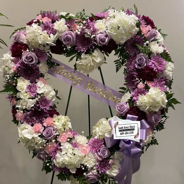 Heart-shaped floral wreath with purple, pink, and white flowers on an easel