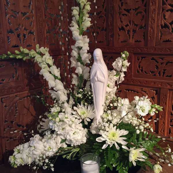 White floral arrangement with a Virgin Mary statue and candle