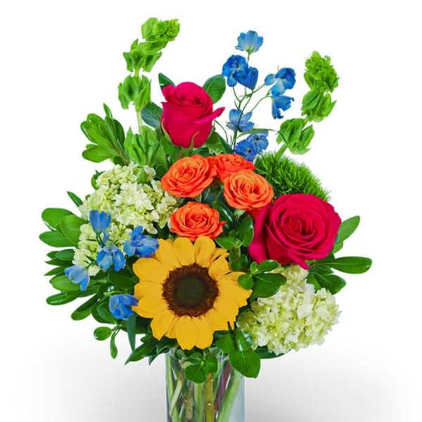 Mixed bouquet in a clear glass vase with roses, sunflower, and blue flowers