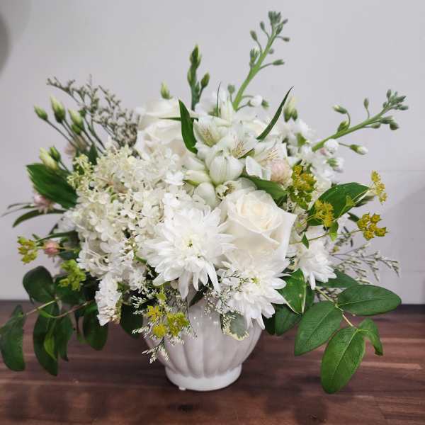 White floral arrangement in a white vase with roses and daisies