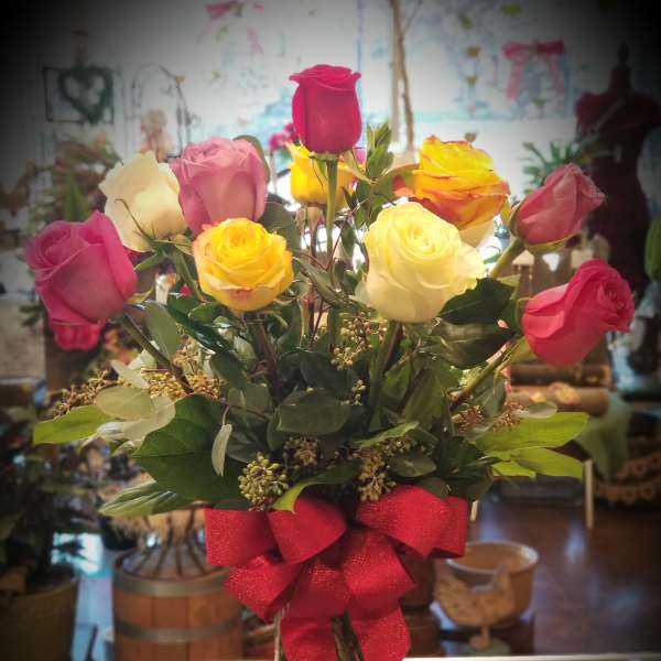Bouquet of multicolored roses in a clear glass vase with a red bow