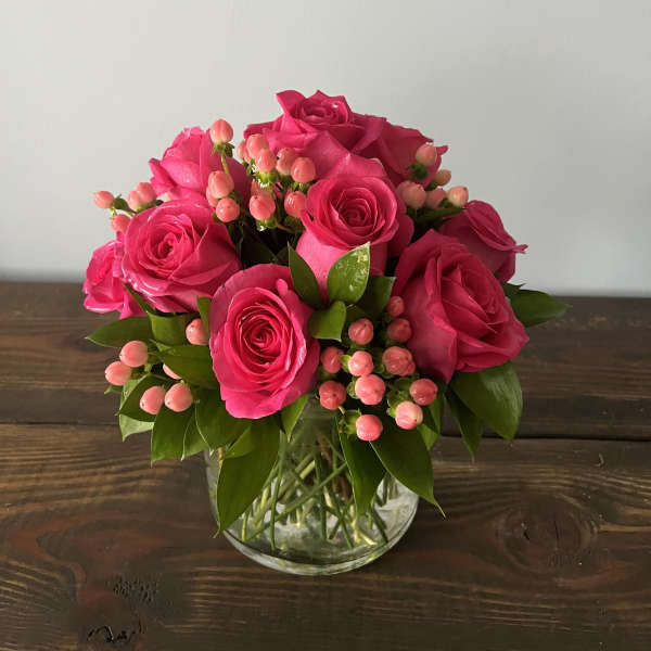 Compact arrangement of bright pink roses and pink berries in a clear glass vase
