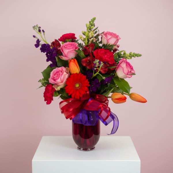 Mixed bouquet of pink, red, purple, and orange flowers in a glass vase