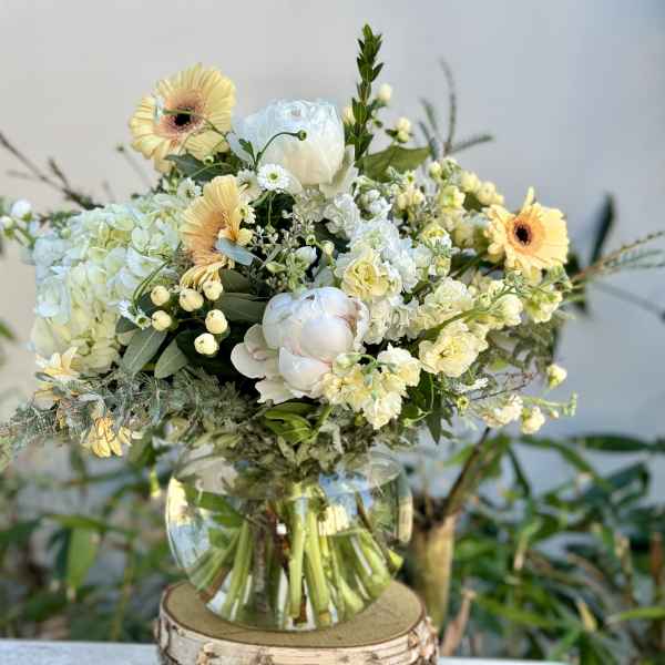 Mixed bouquet of pale yellow and white flowers in a clear glass vase