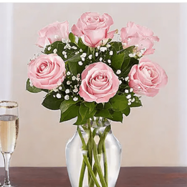 Pink roses with white filler flowers arranged in a clear glass vase on a table.