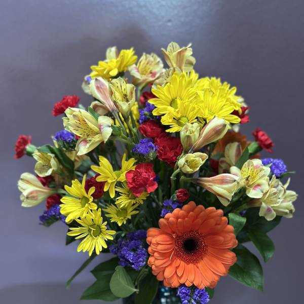 Mixed bouquet with orange gerbera, yellow daisies, and purple filler in a blue vase