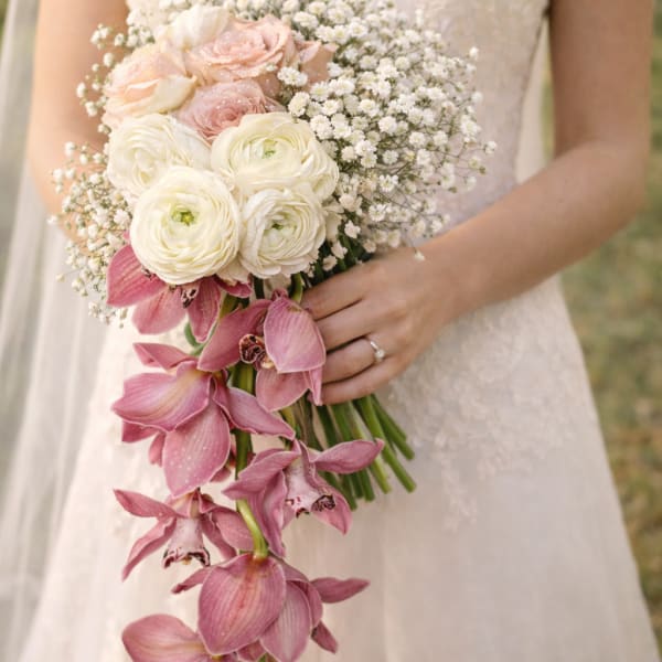Bride holding a bouquet of white and blush flowers with trailing pink orchids