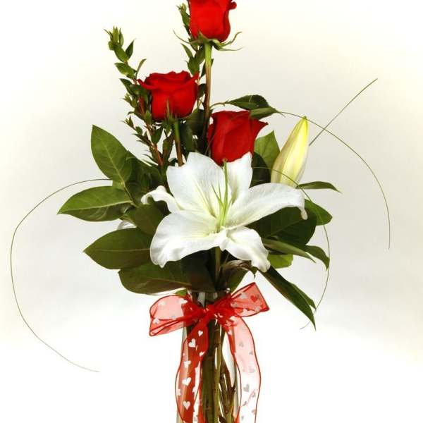 Red roses and a white lily in a clear vase with a red ribbon