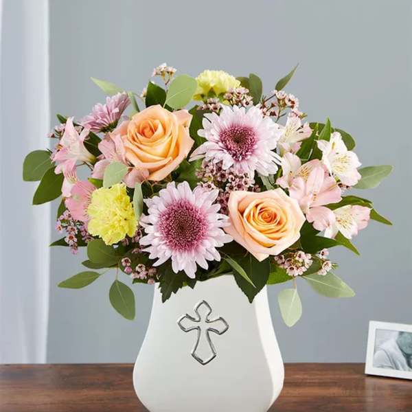 Pastel flower arrangement in a white vase with a cross emblem