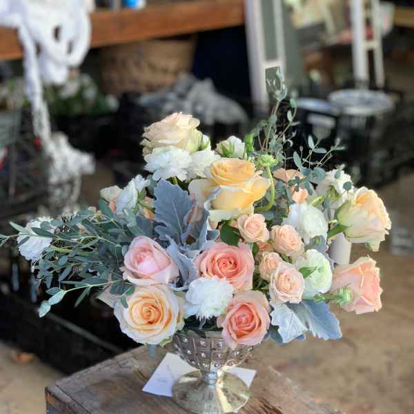 Pastel roses and white blooms arranged in a silver goblet vase
