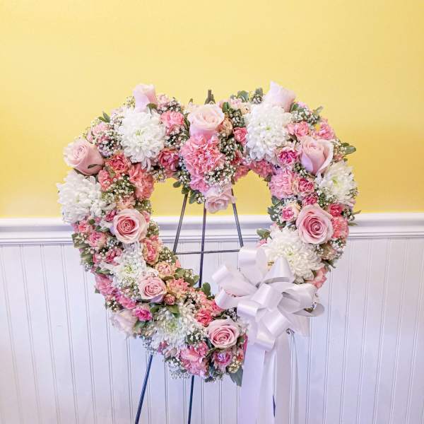 Heart-shaped floral wreath on an easel with pink and white flowers and a white ribbon
