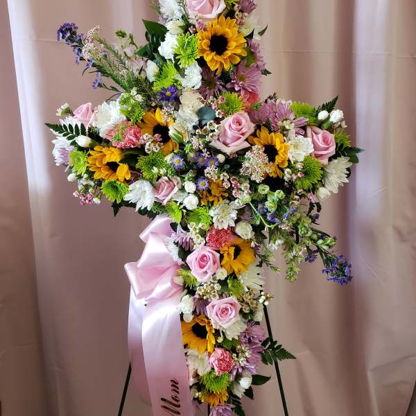Large floral cross with pink roses, sunflowers, and white daisies on a stand