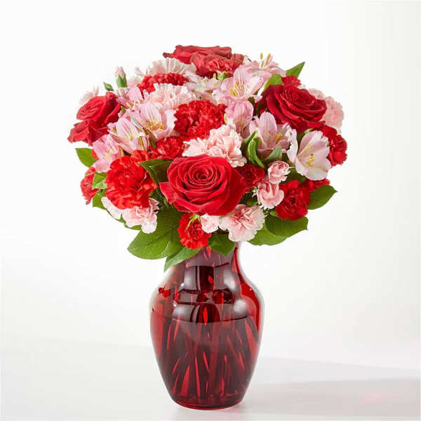 Bouquet of red roses, pink alstroemeria, and carnations in a red glass vase