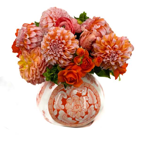 Round arrangement of orange and pink dahlias and roses in a patterned ceramic vase