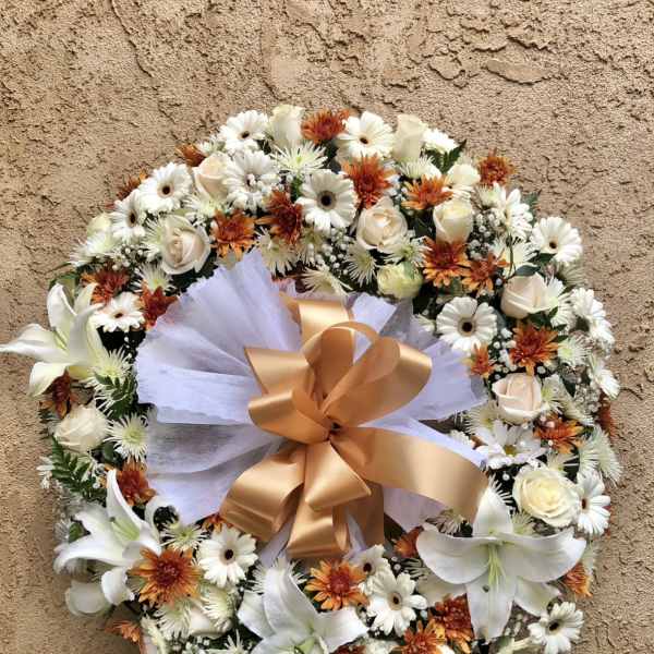 Round floral wreath with white lilies, daisies, and orange blooms on an easel
