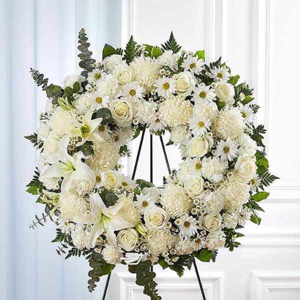 White floral wreath on a black stand with roses, daisies, and lilies