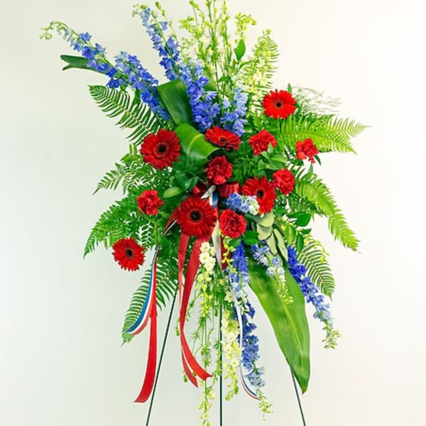 Standing floral spray with red gerberas and blue flowers on a metal easel