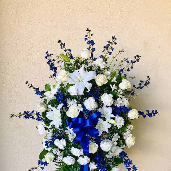 Standing floral spray of white lilies and roses with blue flowers and ribbon