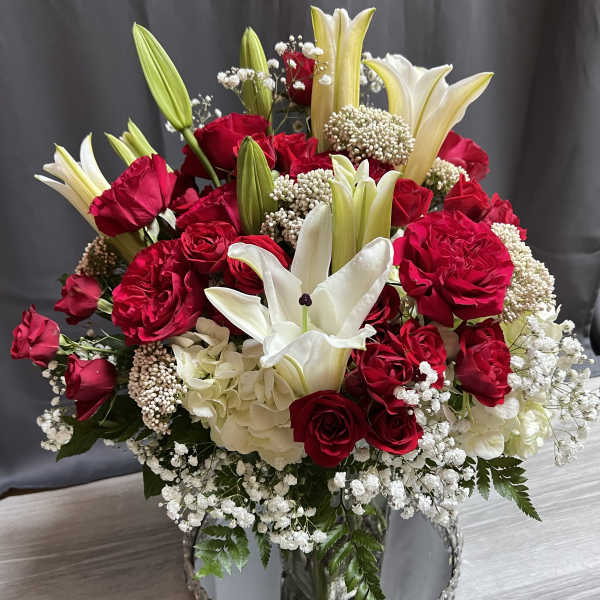 Red roses and white lilies in a mirrored vase with baby's breath