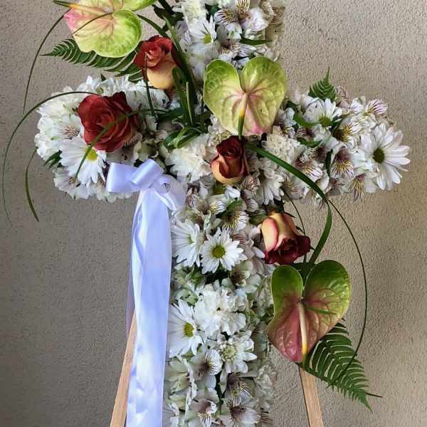 Cross-shaped floral tribute with white daisies and red roses on an easel