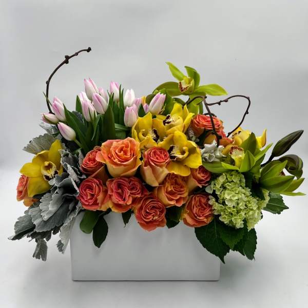 Mixed floral arrangement in a white rectangular vase with roses, orchids, and tulips