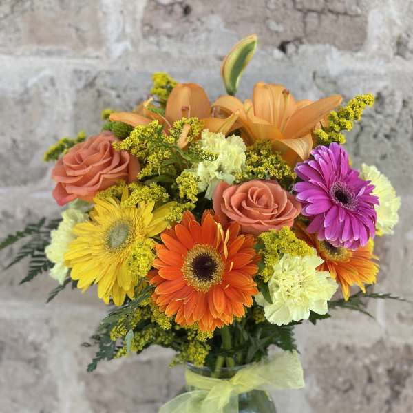 Mixed bouquet of orange, pink, and yellow flowers in a glass vase
