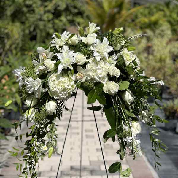 White floral spray on a black stand with trailing greenery