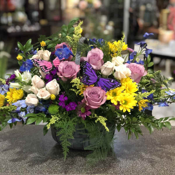 Mixed bouquet of pink roses, yellow daisies, and blue flowers in a black basket