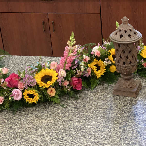 Floral funeral arrangement with sunflowers, pink roses, and snapdragons around a lantern