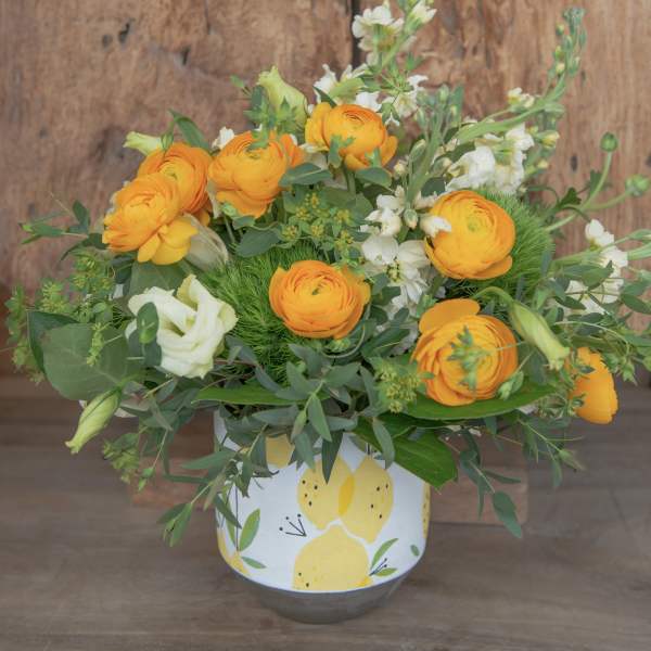 Orange ranunculus and white blooms in a lemon-patterned container