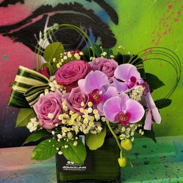 Pink roses and lavender orchids in a black square vase