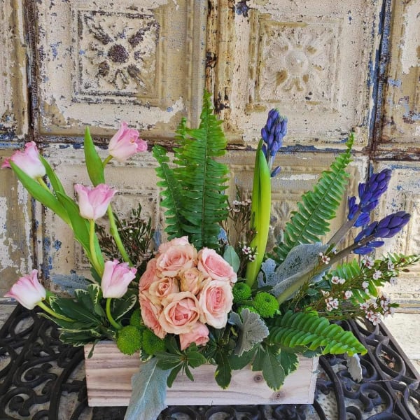 Pink roses and tulips arranged in a wooden box with purple blooms