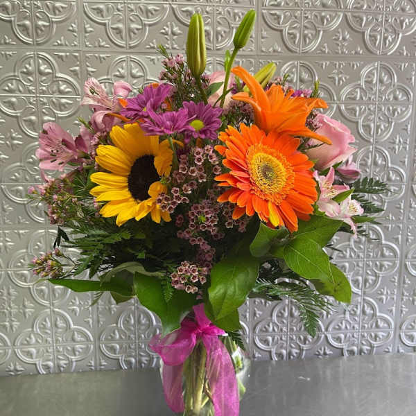 Mixed bouquet with sunflowers, gerbera daisies, and pink lilies in a glass vase