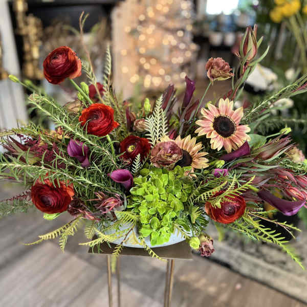 Low floral arrangement with red ranunculus, sunflowers, and purple calla lilies