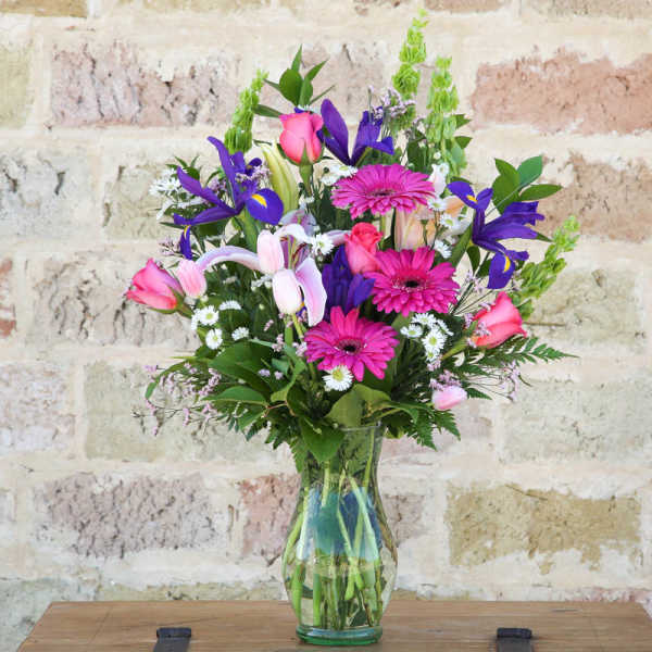 Mixed bouquet of pink, purple, and white flowers in a clear glass vase