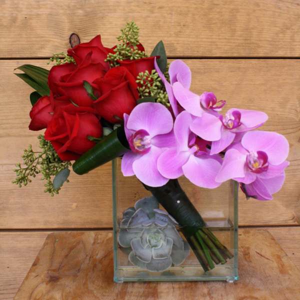 Red roses and pink orchids in a glass cube vase with succulents
