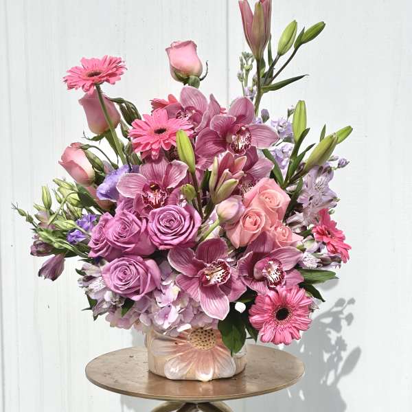 Pink roses, orchids, and gerbera daisies arranged in a ceramic vase