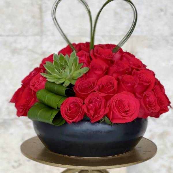 Heart-shaped red rose arrangement in a black bowl with a green succulent accent