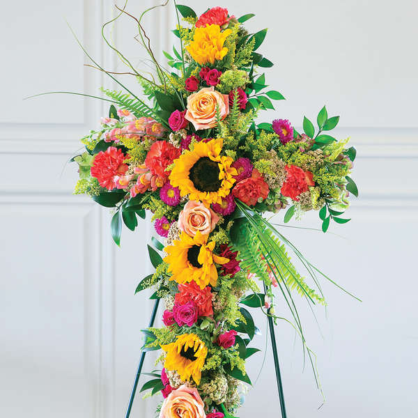 Tall floral cross on a stand with sunflowers, roses, and carnations